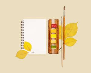 Watercolor Set, Brushes And Blank Sketchbook With Autumn Leaves On Beige Background. Concept Of Fall Creativity, Seasonal Art Projects, Autumn DIY Ideas, Back To School, And Artistic Inspiration
