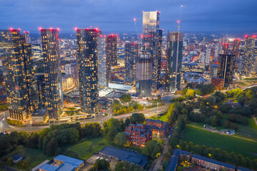 Aerial view of Deansgate Square towers and Manchester skyline glowing at night with illuminated streets below.