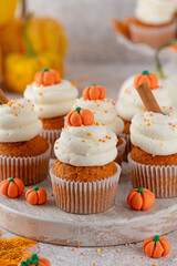 Pumpkin spice cupcakes decorated butter cream frosting, sugar sprinkles and mini sweet pumpkins on top. Thanksgiving or Halloween dessert.