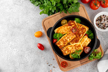 Fried halloumi cheese in a cast iron skillet with parsley and tomatoes on a concrete background. Top view.