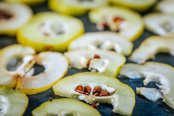 Thinly sliced yellow quince rings arranged on a dark surface, some with seeds still visible, highlighting the fruit's pale interior and circular shapes.