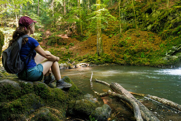 A tourist sitting by a river in the forest in Besse-et-Saint-Anastaise, Auvergne
