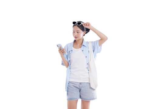 Traveler in Casual Attire: A young traveler, dressed in a stylish ensemble with sunglasses perched atop her head, checks her phone while holding a shoulder bag.