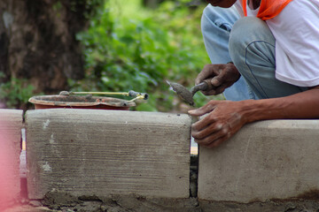 A construction worker, wearing an orange safety vest, precisely installs concrete kerbstones using a trowel, emphasizing manual construction and detail.