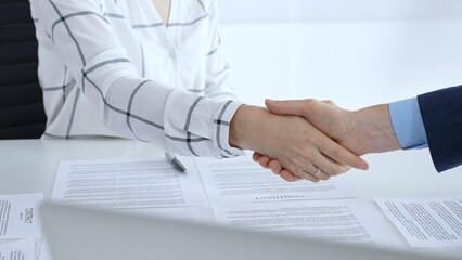 Business people shaking hands over contract documents and laptop, confirming successful partnership, agreement, or merger in a corporate office meeting