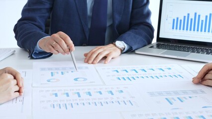 Business people collaborating at a conference table, reviewing financial charts and reports, using a laptop and calculator while engaging in discussions about strategy and performance. Accouters at
