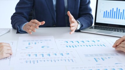 Business people reviewing financial charts and reports in office, using a laptop and calculator while engaging in discussions about strategy and performance