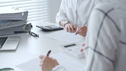 Two unrecognizable accountants collaborating in a well lit office, analyzing financial data and preparing reports with calculators and pens. Audit and taxes concept