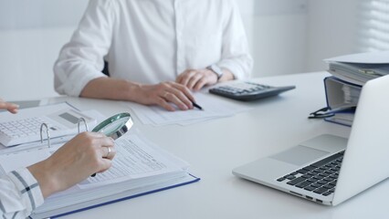Team of accountants are working together, using a magnifying glass and a calculator, to audit financial reports in office. Audit and taxes in business