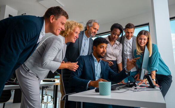 Diverse business team collaborating around a desktop computer, engaged in focused discussion and analysis in a modern office, demonstrating teamwork, planning and problem-solving