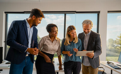 Diverse business team collaborating and discussing a project using a digital tablet, sharing ideas and expertise in a bright, contemporary office environment