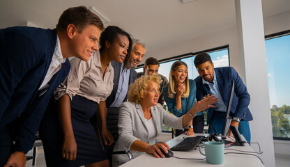 Diverse business professionals gathering around a computer, discussing data on the screen and collaborating on a new project in a modern office environment