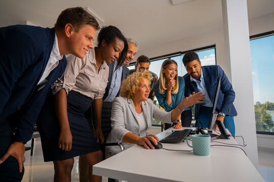 Diverse business team collaborating around a computer monitor in a modern office, sharing ideas, smiling and strategizing during a productive meeting and brainstorming session
