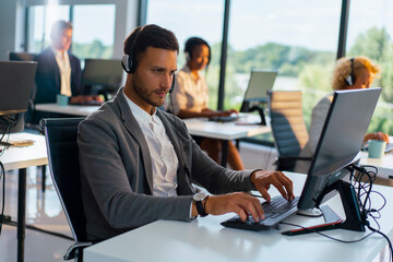Call center operator wearing a headset and working intensely on a computer, providing customer service while working with colleagues in a modern office environment