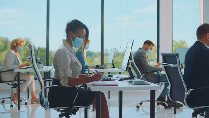 Office workers wearing medical masks and keeping social distance are working diligently at their individual desks, adapting to new normal workplace protocols in a modern corporate environment