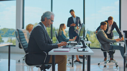 Diverse business people actively working and collaborating on computers in a bright, modern office space, fostering teamwork and professional productivity during daytime