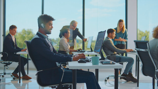 Diverse business professionals collaborating and focusing on their work at individual workstations, analyzing data and communicating with headsets in a bright corporate environment