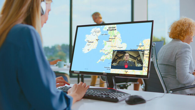 Woman wearing headphones types at a keyboard during a video conference, monitoring a united kingdom map on her screen to illustrate remote collaboration and global business communication