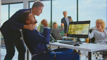Diverse business team cheering and fist pumping, celebrating a successful trade on a computer screen displaying bitcoin and financial charts in a modern office