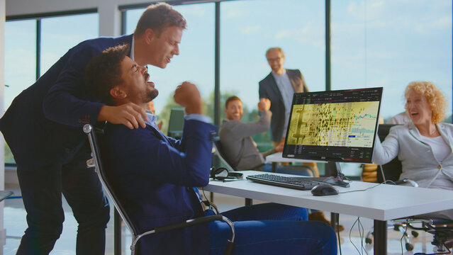 Diverse business team cheering and fist pumping, celebrating a successful trade on a computer screen displaying bitcoin and financial charts in a modern office - Powered by Adobe