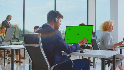 Multiracial team of call center customer service operators wearing headphones, working on computers with customizable green screens in a modern, bright corporate office