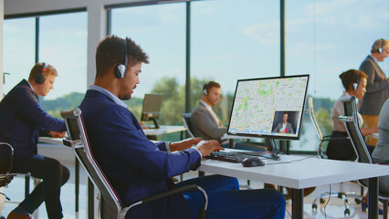 Diverse customer service team members are working at their desks, providing support through headsets and computers, with one consultant engaging in a video call displaying a map on his screen