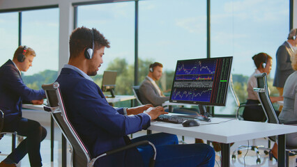 Business people working in a modern office, wearing headsets and actively monitoring financial data, stocks, charts, and graphs on computers, analyzing market trends