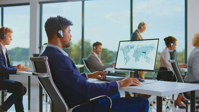 Diverse customer service agents wearing headsets and working on computers with a world map displaying on screens, providing global support in a modern office