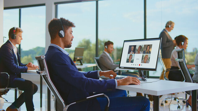 Diverse business professionals wearing headsets and collaborating in a video conference call, working on computers in a contemporary shared office space