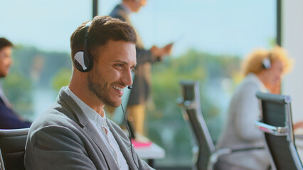 Man smiling, wearing a headset, providing customer service and support in a corporate call center environment, actively engaging in communication with clients