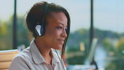 Black woman in modern office wearing headset, smiling and focused while providing customer support;...