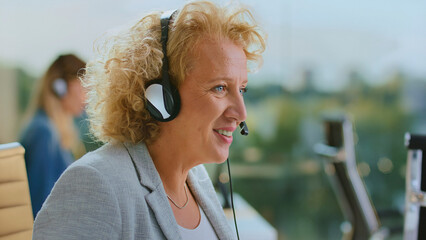 Smiling senior woman wearing a headset and microphone, providing customer service and support in a...