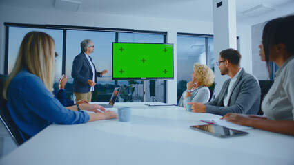 Fototapeta premium Business executive presenting a new project idea or marketing strategy on a large chroma key display to a diverse group of attentive colleagues during a modern office meeting