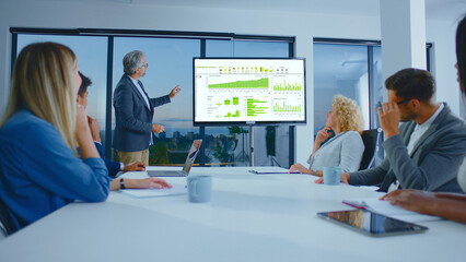 Business professional leading a corporate meeting, presenting financial data and charts on a large...
