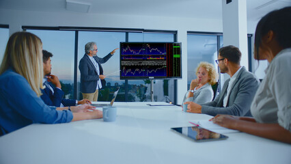 Business professionals are attentively discussing charts and graphs on a large screen, focusing on finance, stock market trends, and economic data during an intense corporate meeting