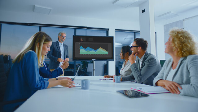 Diverse business people attending a corporate meeting in a modern conference room, watching a senior manager presenting data charts on a screen, fostering teamwork and professional collaboration