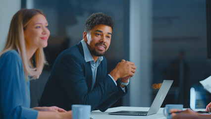 Diverse business professionals in a modern office engaged in a collaborative meeting, listening,...