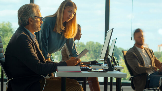 Business colleagues collaborating on an important project, the experienced male mentor guiding and explaining complex information to the younger female professional in a modern office environment - Powered by Adobe