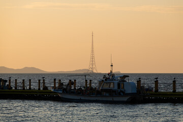 Fototapeta premium idyllic seascape with island, pylon and pier during sunset