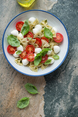 Plate of caprese pasta salad with farfalle, vertical shot on a beige and grey granite background with space, view from above
