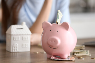 Piggy bank with money on table against woman in kitchen, closeup