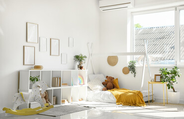 Interior of light children's room with blank frames, shelf unit and bed