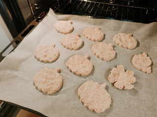 Pumpkin and leaf shaped biscuits baking in oven on baking paper