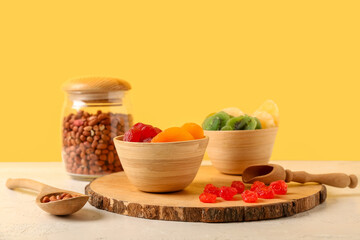 Wooden bowls with different candied fruits and jar of peanuts on white table