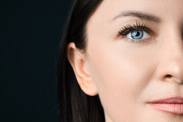 Fototapeta premium Beautiful young woman with blue eyes on black background, closeup