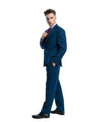 side view of confident young businessman adjusting tie and posing