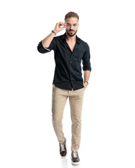 sexy casual man in black shirt fixing glasses and walking with hand in pocket