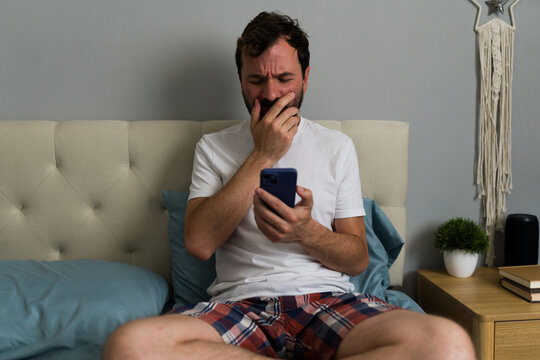 Man sitting on bed crying after reading bad news on smartphone
