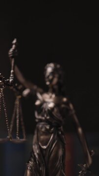 vertical video of bronze law statue represented by blindfolded goddess spinning and holding a balance signifying impartiality and two broad sources of law with flash lights on 