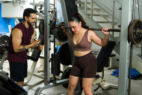 Woman squatting with barbell, personal trainer coaching workout